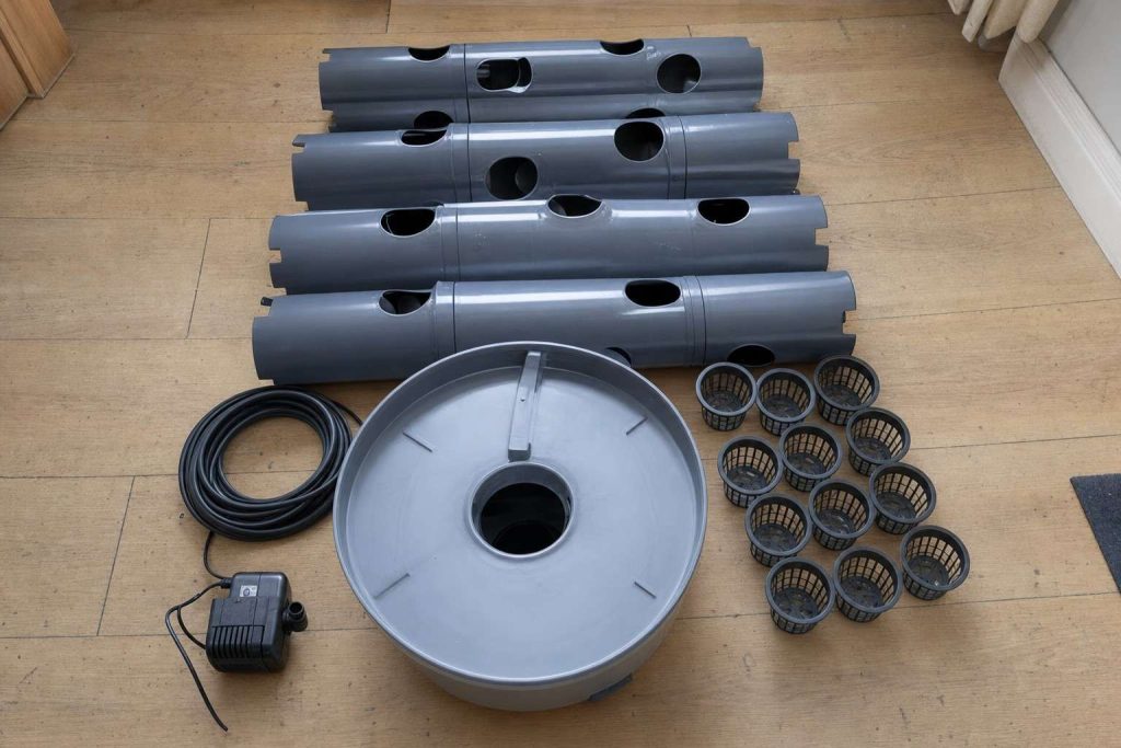 Tower garden column sections, net pots, pump and tubing laid out on a wooden floor ready for assembly