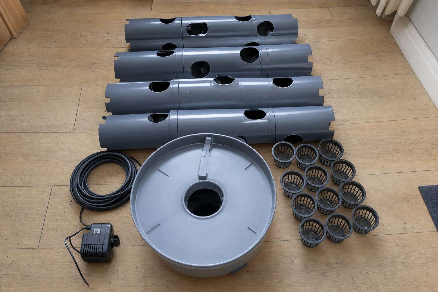 Tower garden column sections, net pots, pump and tubing laid out on a wooden floor ready for assembly
