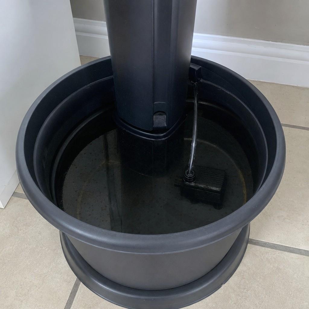 Small submersible pump and water reservoir at the base of a hydroponic tower garden on a tiled floor