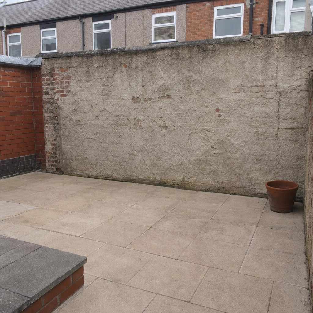 Empty small paved UK patio with bare concrete walls and a single empty pot in the corner