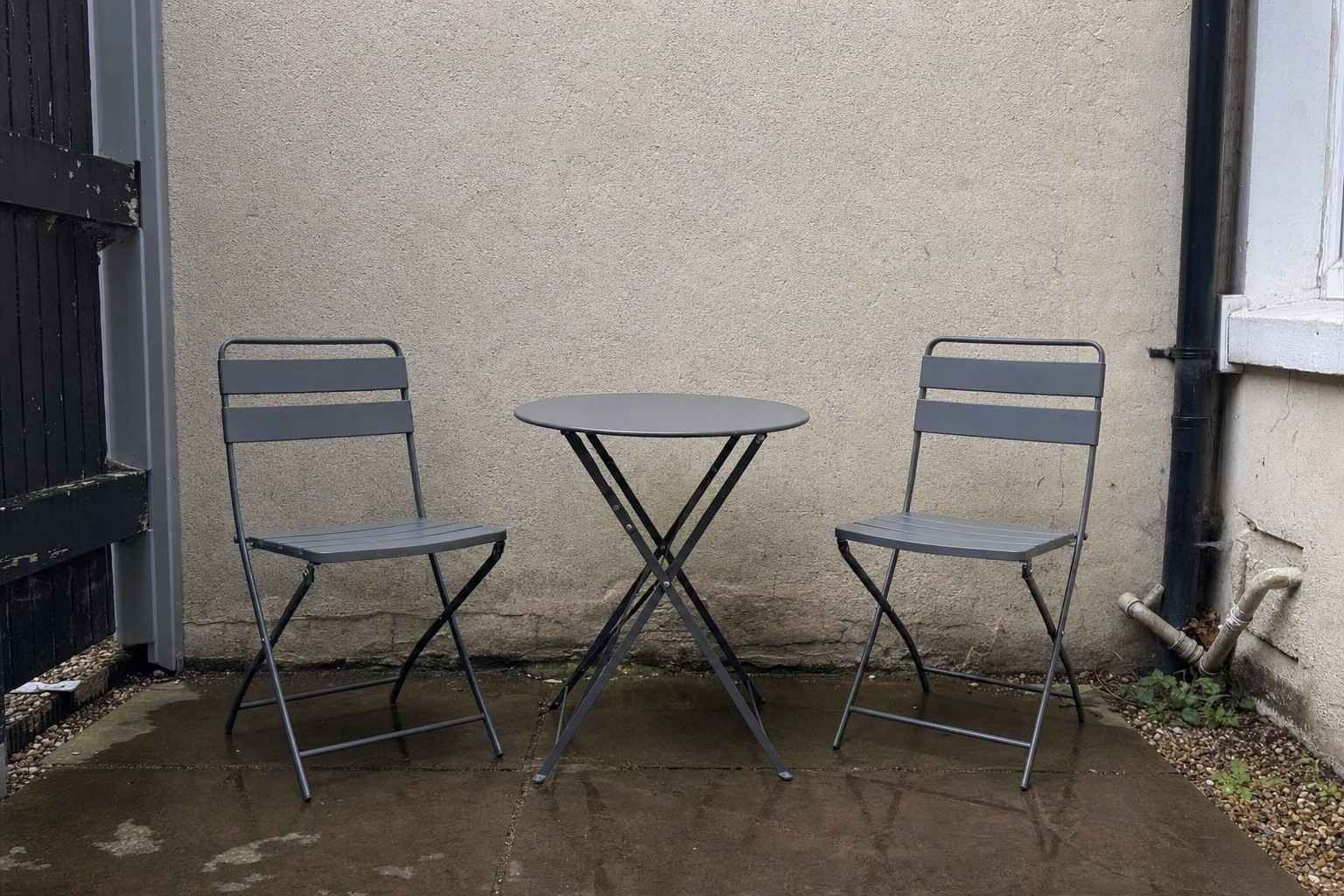 A small plain bistro table and two chairs on a narrow UK patio, viewed from the front